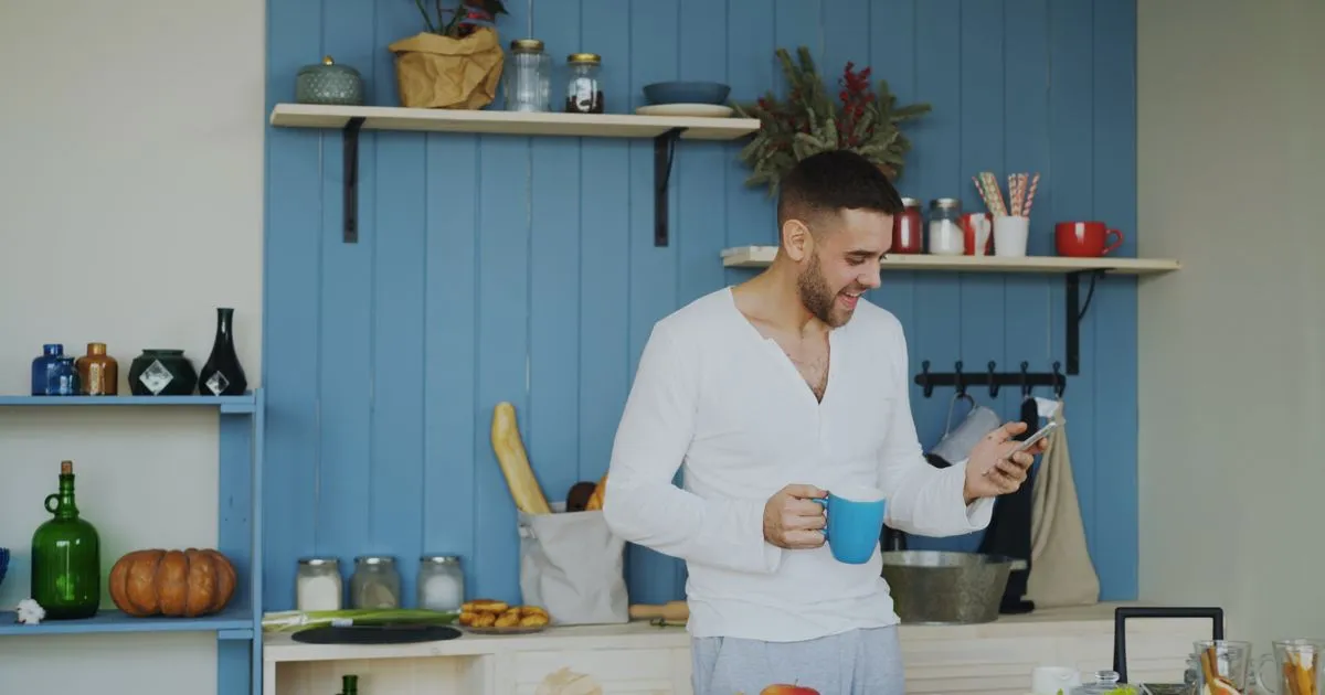 Man checking his phone in the kitchen as an e-transfer loan arrives in Canada
