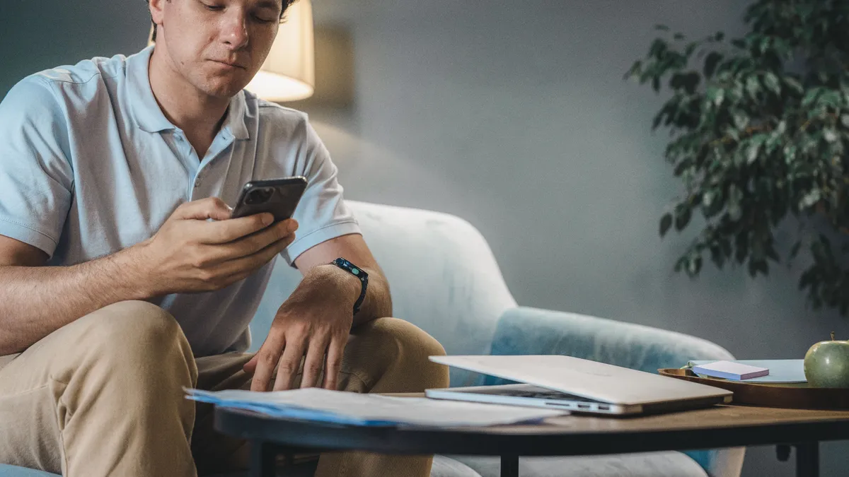 Man on a sofa applying for personal loans on his phone with a laptop open